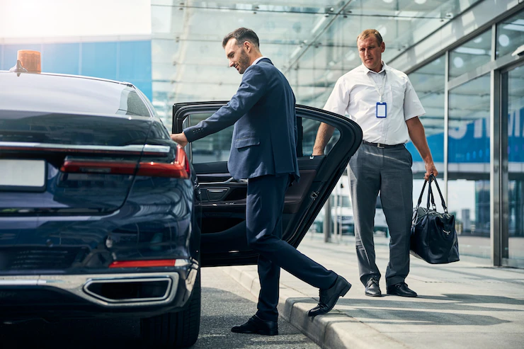 well-dressed-male-traveler-getting-into-taxi-while-porter-holding-his-duffel-bag-standing-by-car_447912-5397